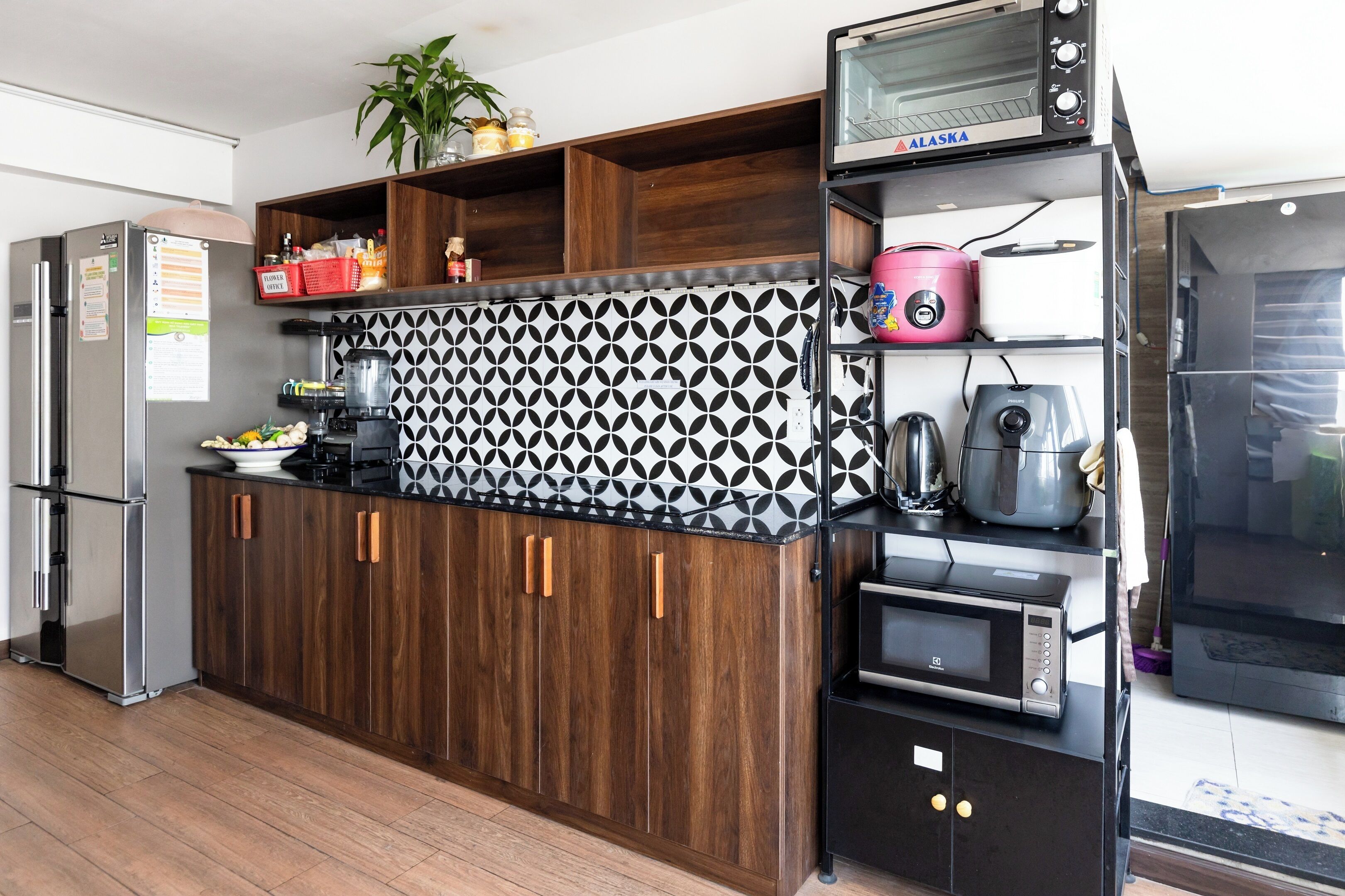 A modern kitchen with a built-in oven, microwave, and coffee maker. There is a refrigerator and a wooden cabinet with a patterned backsplash.