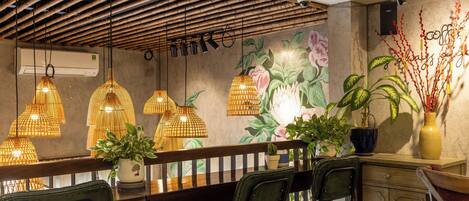 Interior de restaurante con techo de bambú, lámparas colgantes y decoración floral en las paredes.