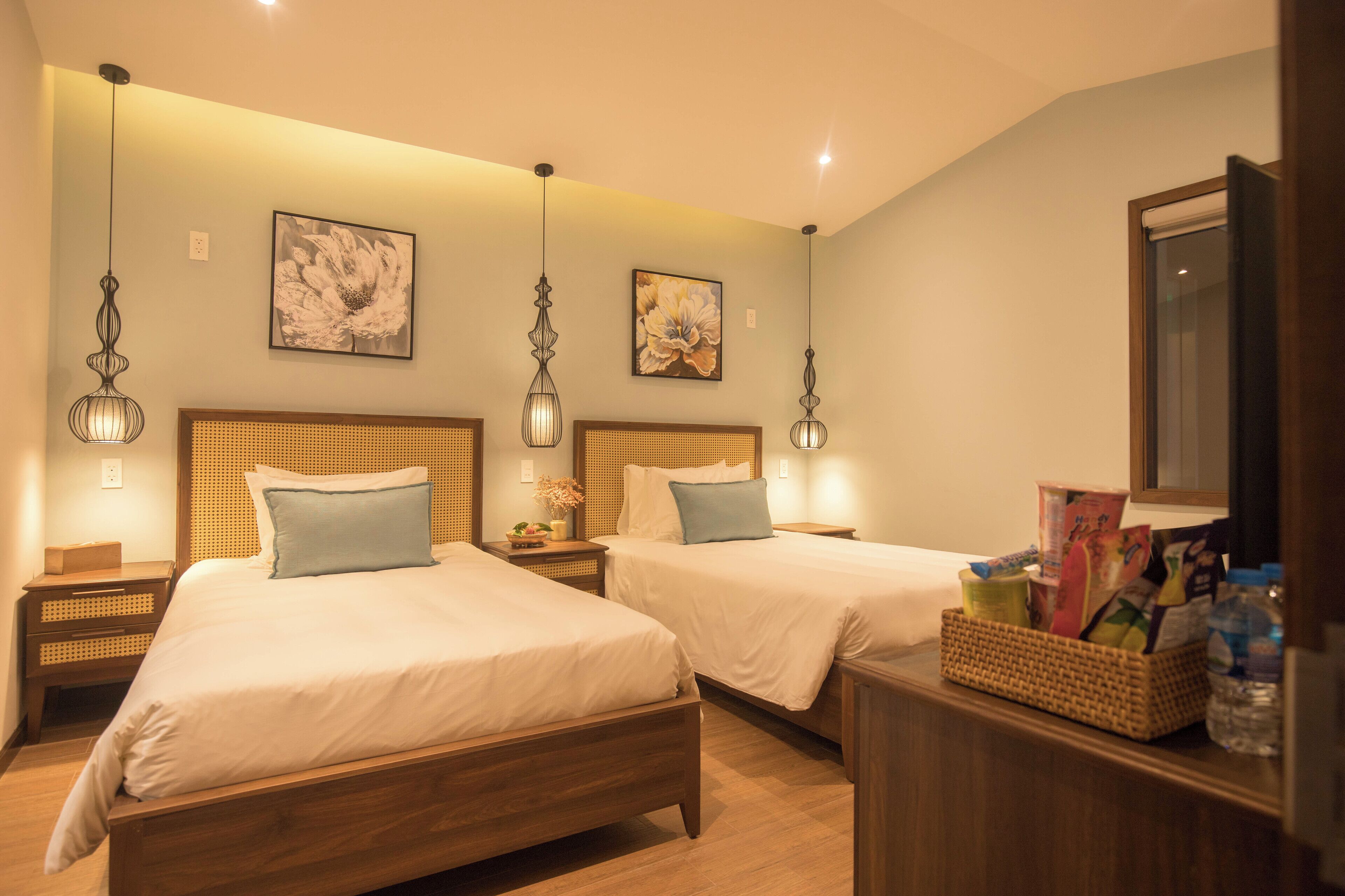 Een hotelkamer met twee houten bedden, een nachtkastje met een lamp en een rieten mand ernaast.