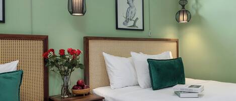 A hotel room with two beds, a rattan headboard, a vase with red flowers, and a framed artwork on the wall.