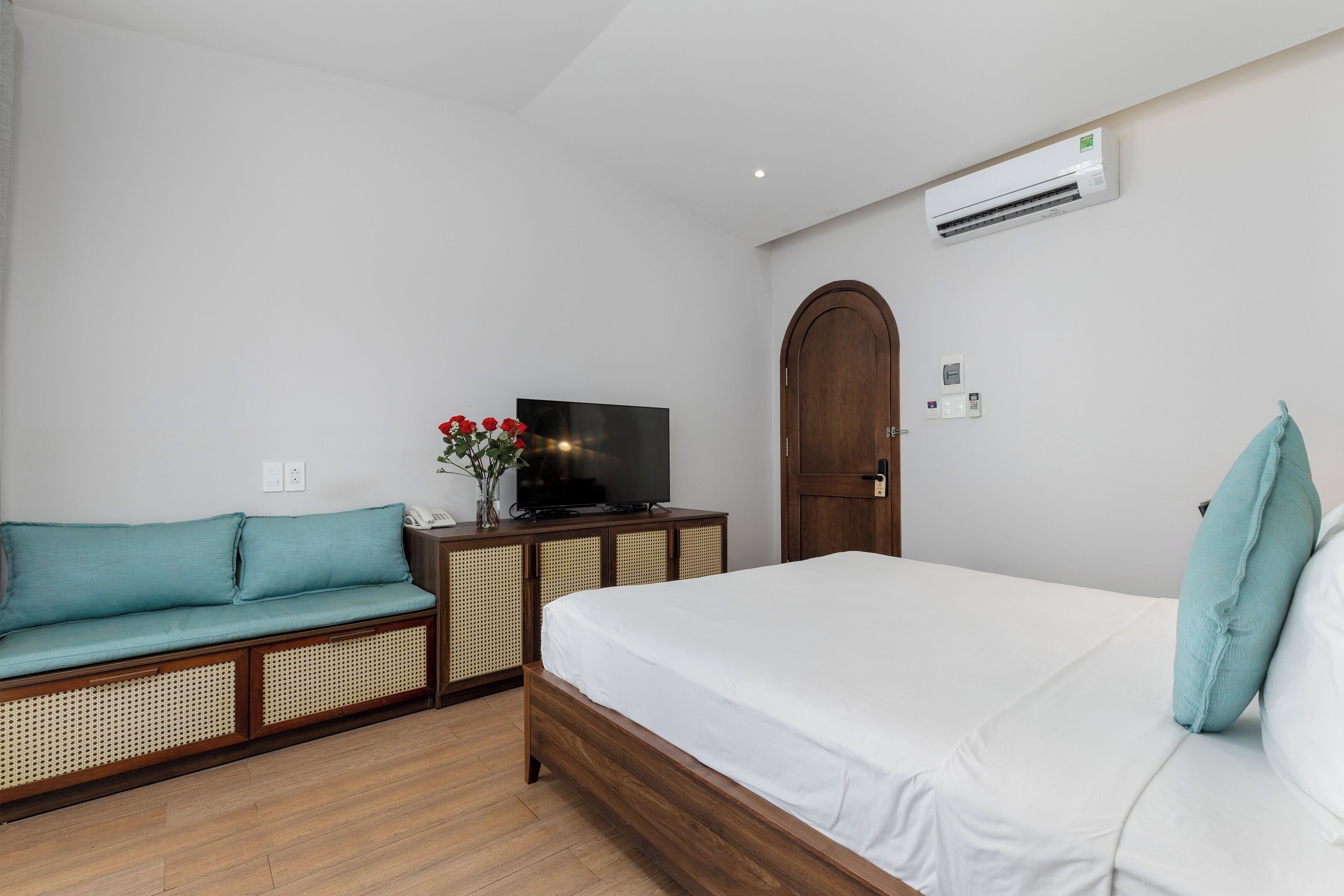 A bedroom with a bed, a sofa, a television, and an air conditioning unit.