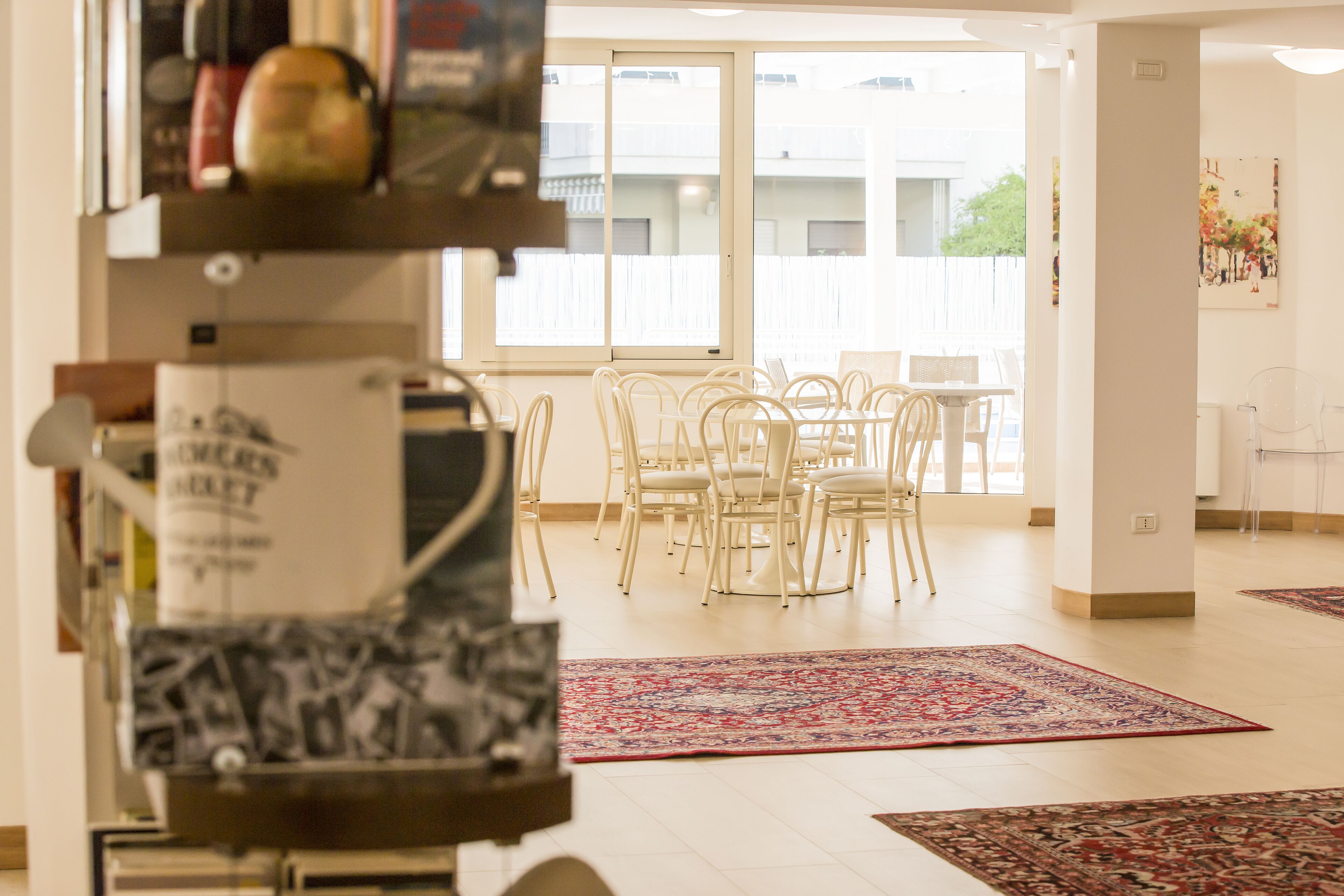 A spacious room with a dining area featuring white chairs and a large window.