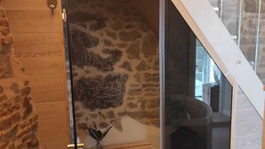 A modern interior with a stone wall, a wooden bench, and a glass door leading to a dark room. - San Michele al Castello (Castiglion Fiorentino)