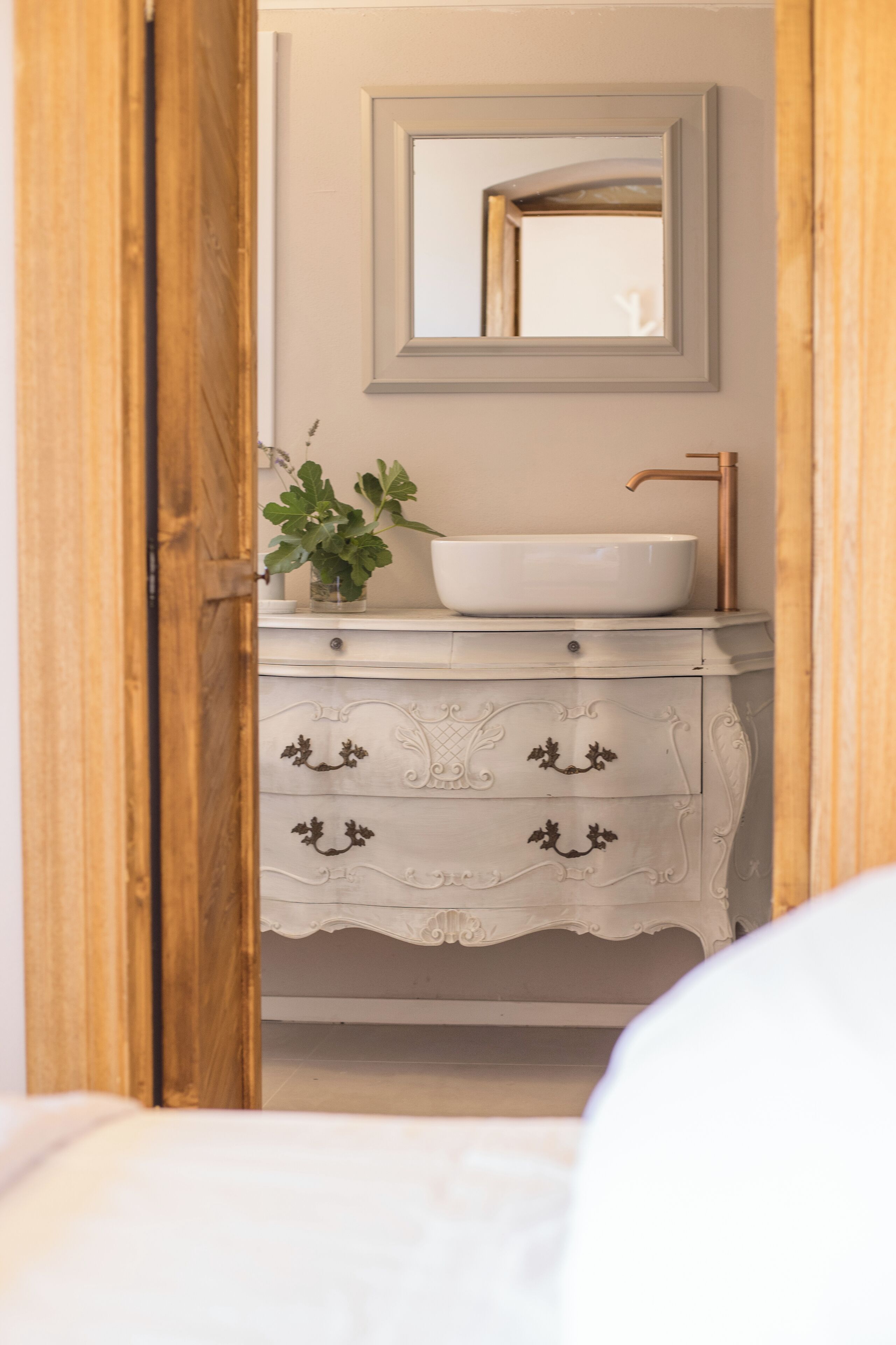 Een badkamer met een wit wastafelmeubel, een spiegel en een houten deur.