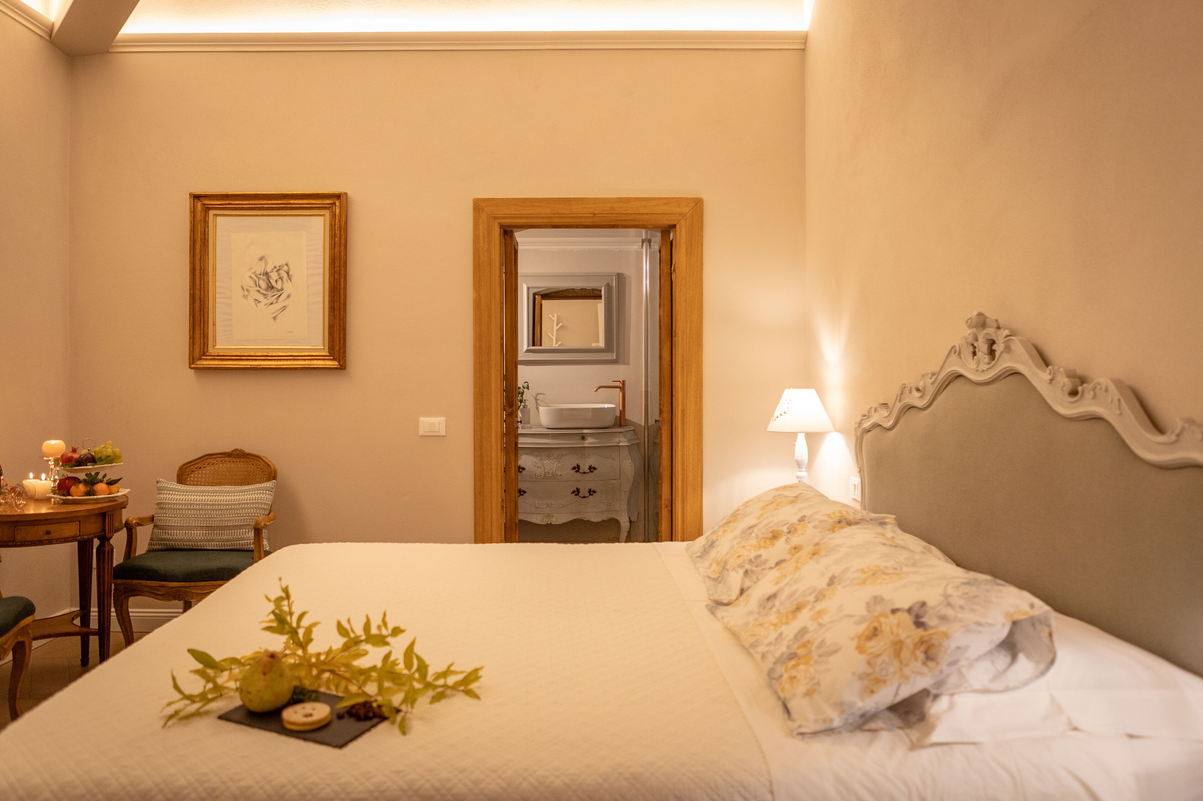 Quarto de hotel com cama bem arrumada, mesa de cabeceira com abajur, quadro na parede e porta de acesso a um banheiro.