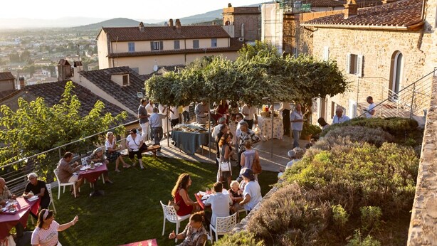 An outdoor event with people seated at tables, surrounded by stone buildings and greenery. - San Michele al Castello (Castiglion Fiorentino)