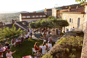 An outdoor event with people seated at tables, surrounded by stone buildings and greenery. - San Michele al Castello (Castiglion Fiorentino)