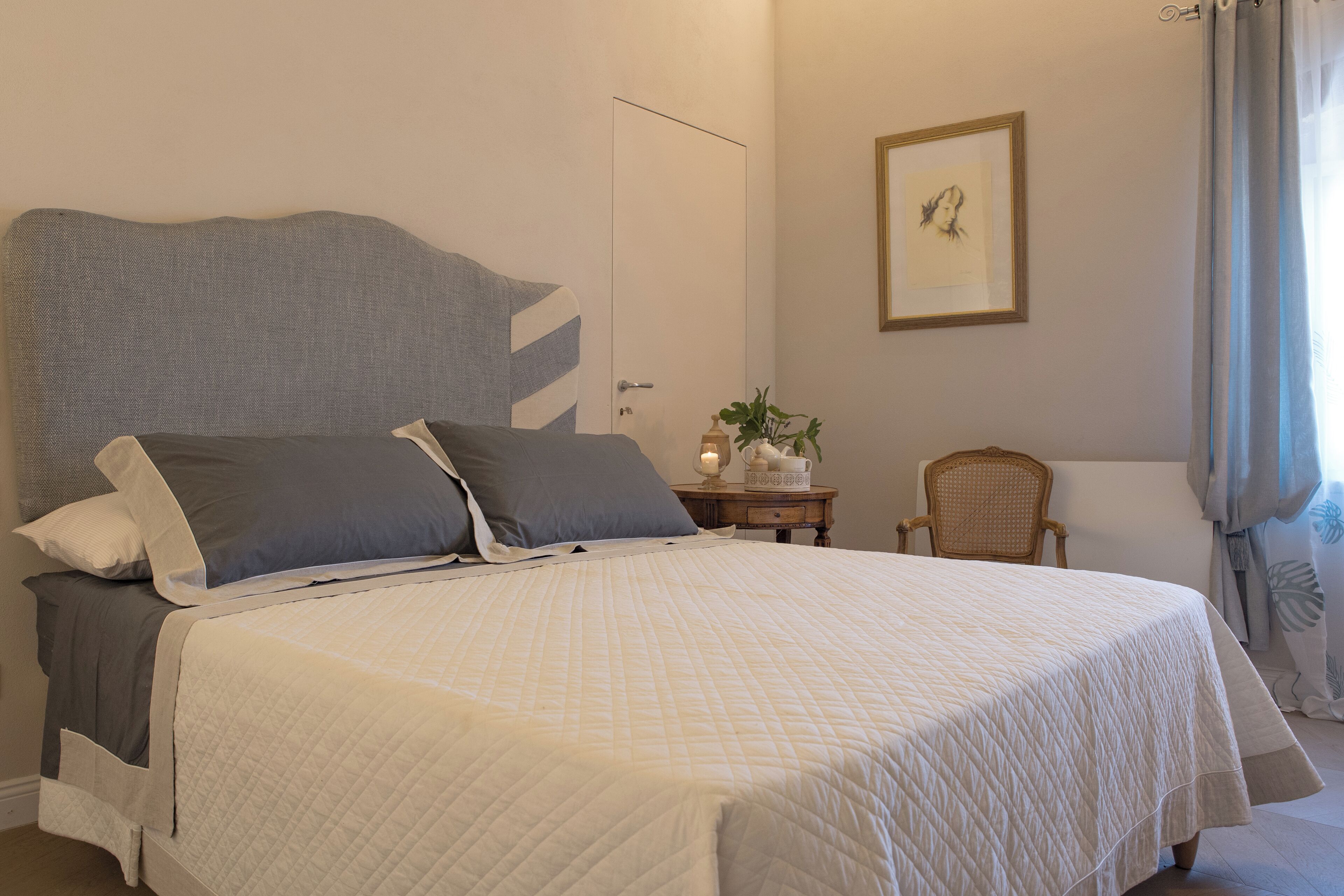 A neatly made bed with a quilted white cover, a grey headboard, and two pillows.