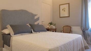 A neatly made bed with a quilted white cover, a grey headboard, and two pillows.