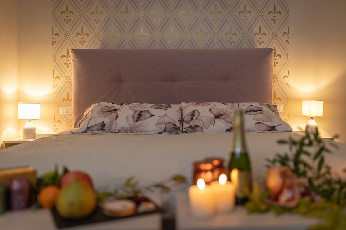 A neatly made bed with floral bedding, two bedside lamps, and a fruit arrangement on the nightstand.