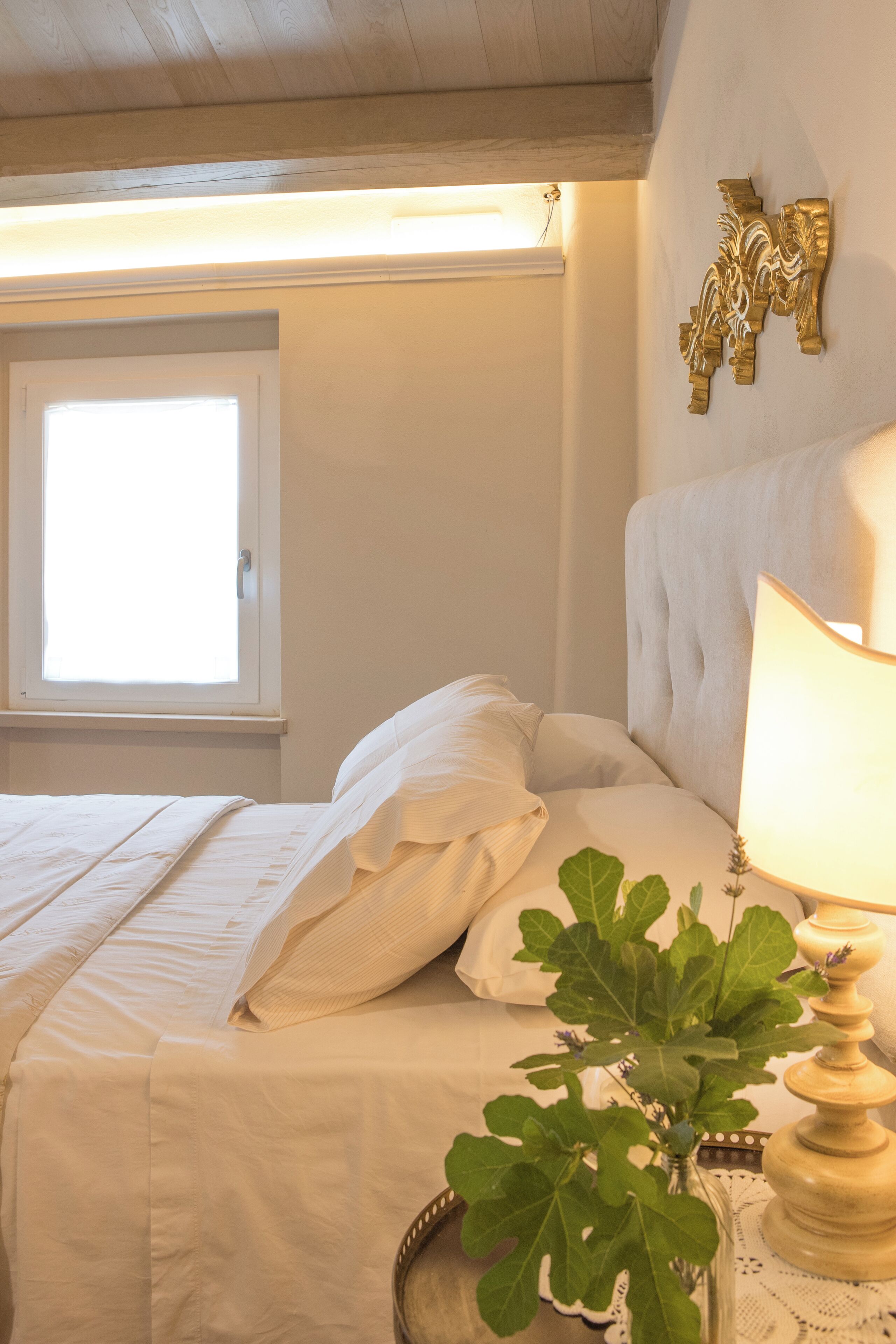 A neatly made bed with white linens, a bedside lamp, and a decorative wall piece.