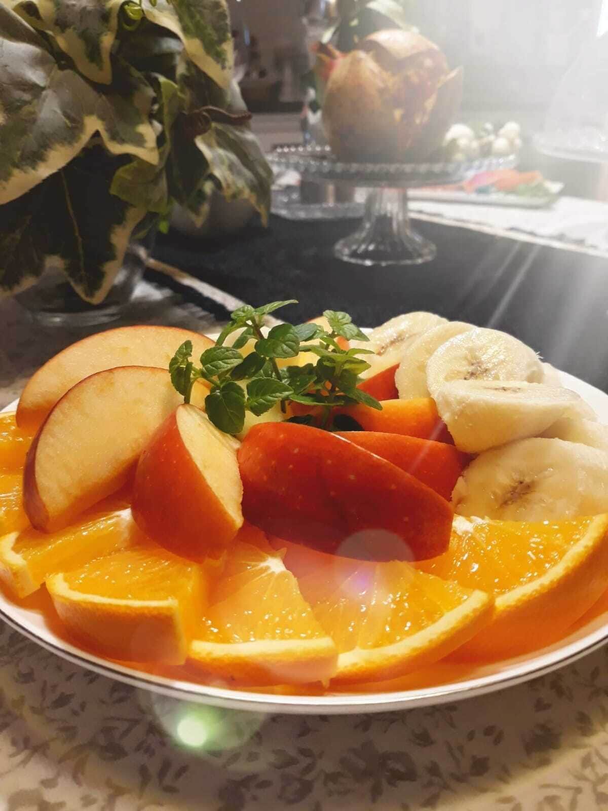 Un plato de frutas cortadas, incluyendo manzanas, plátanos y naranjas, decorado con hojas de menta.