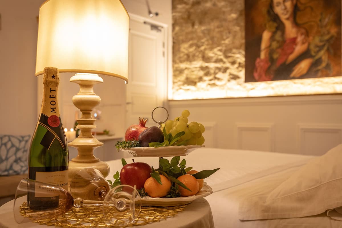 A table with a bottle of champagne, a glass, a fruit platter, and a candle.