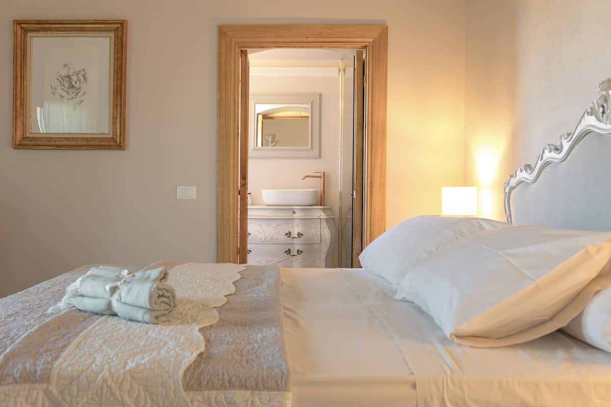 A hotel room with a bed, a bedside table, a mirror, and a bathroom with a sink and towel rack.