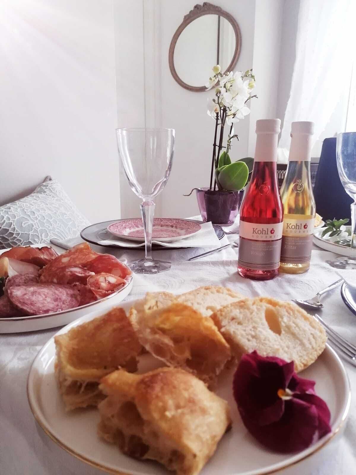 A dining table with plates of food, wine bottles, and a vase of flowers.