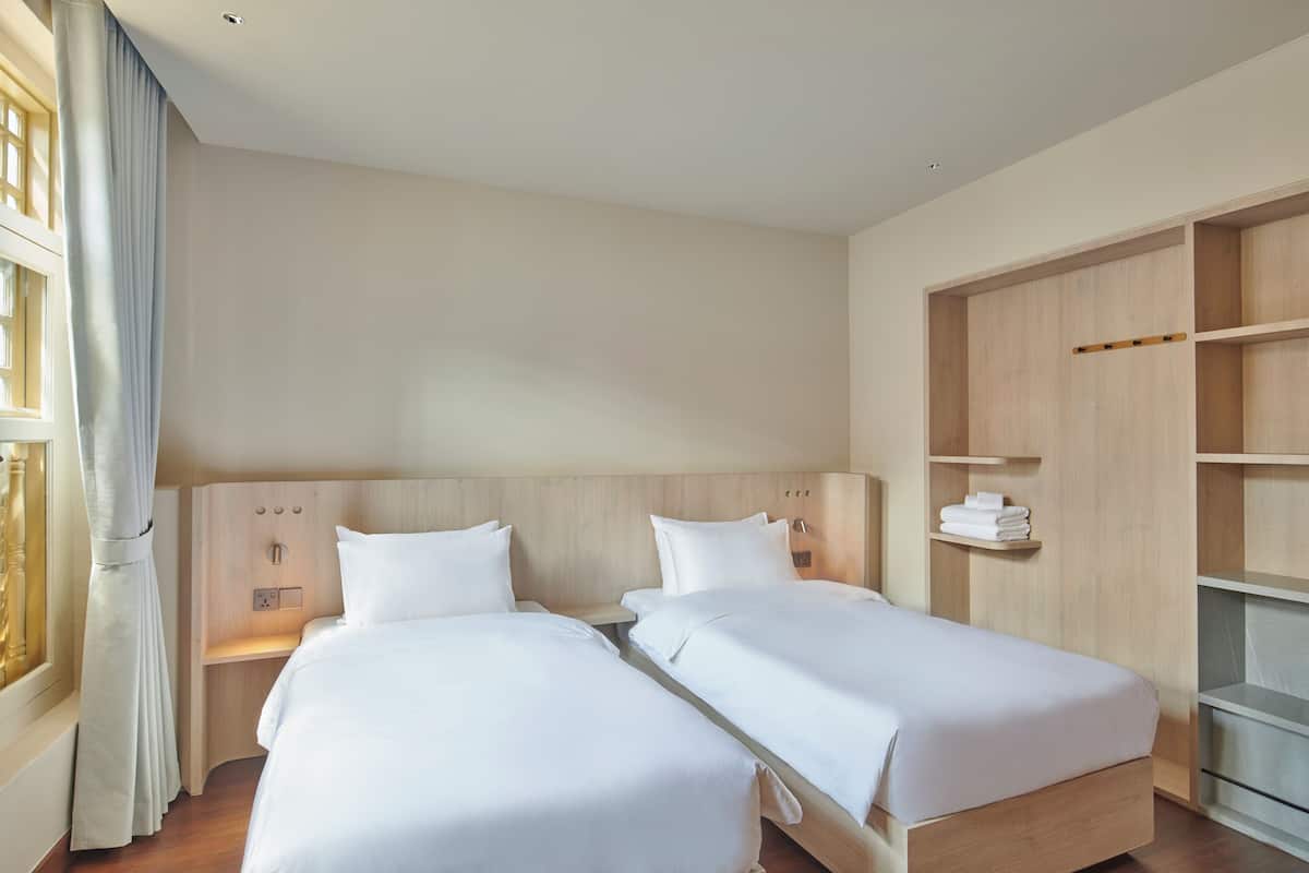 A hotel room with two beds, a wooden headboard, a built-in wardrobe, and a window with curtains.