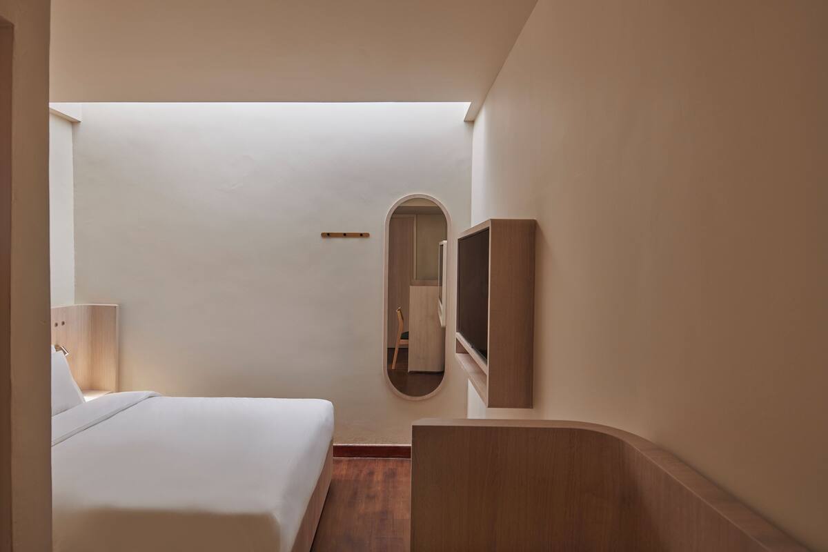 A hotel room with a bed, a mirror, a TV, and a wooden desk.