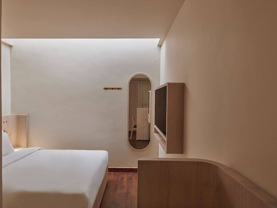 Habitació d'hotel amb un llit, un mirall, un televisor i un escriptori de fusta.