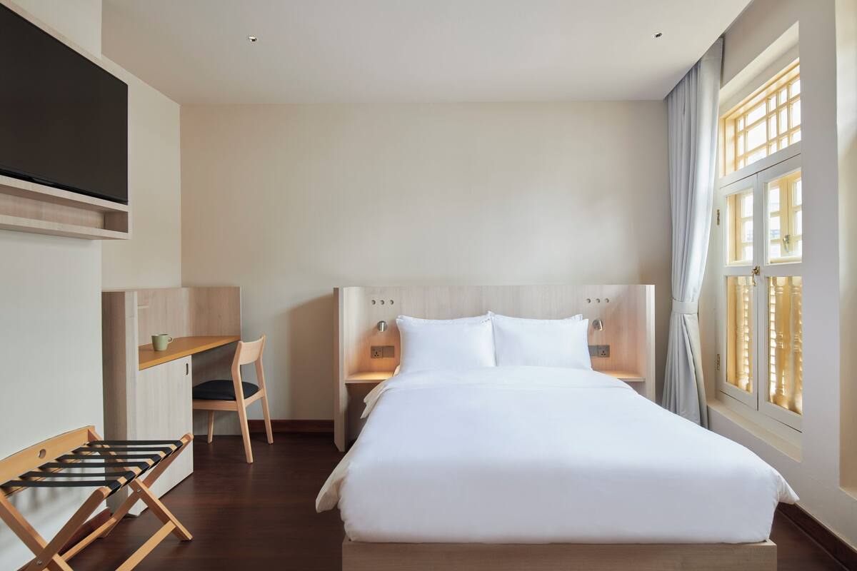 A hotel room with a bed, a desk, a chair, and a TV.