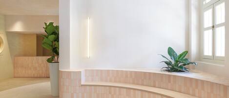 Un área de recepción moderna con un mostrador curvo, una planta en maceta y un amplio ventanal que proporciona luz natural.