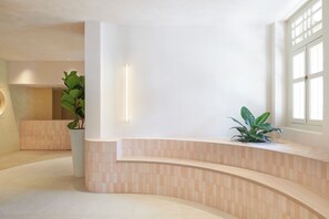 A modern reception area with a curved reception desk, a potted plant, and a large window providing natural light. - KINN Studios (Singapore)