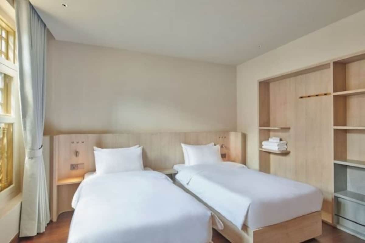 A hotel room with two single beds, a wooden headboard, a built-in wardrobe, and a window with curtains.
