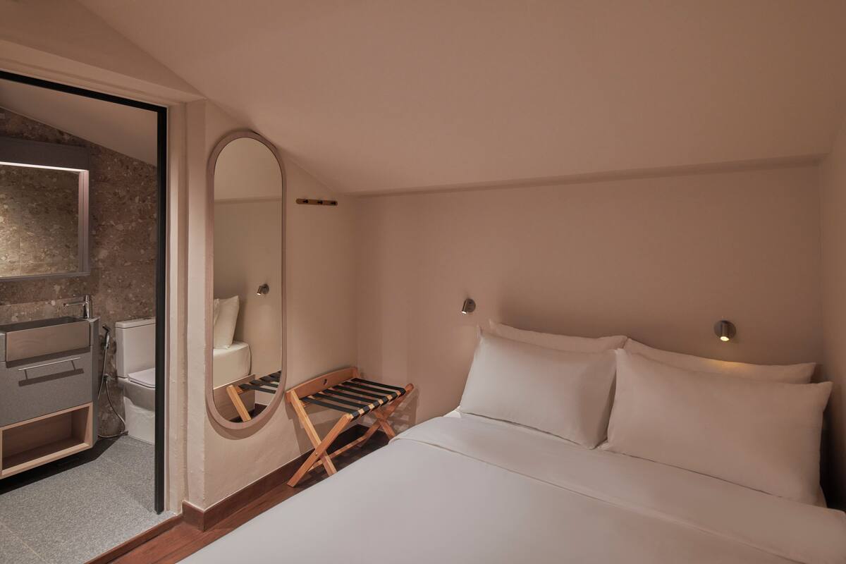 A bedroom with a bed, a wooden bench, a mirror, and a toilet.