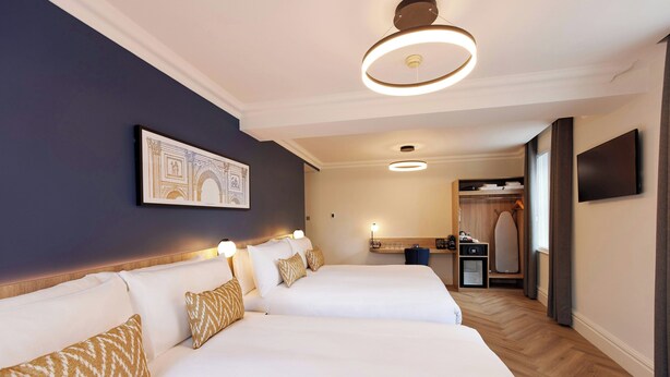 A hotel room with two beds, a flat-screen TV, a mirror, a desk, and a wardrobe. - Thistle London Park Lane (London)