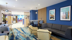 A modern lounge area with a blue accent wall, a sofa, chairs, a small table, and a wall-mounted TV. - Thistle London Park Lane (London)