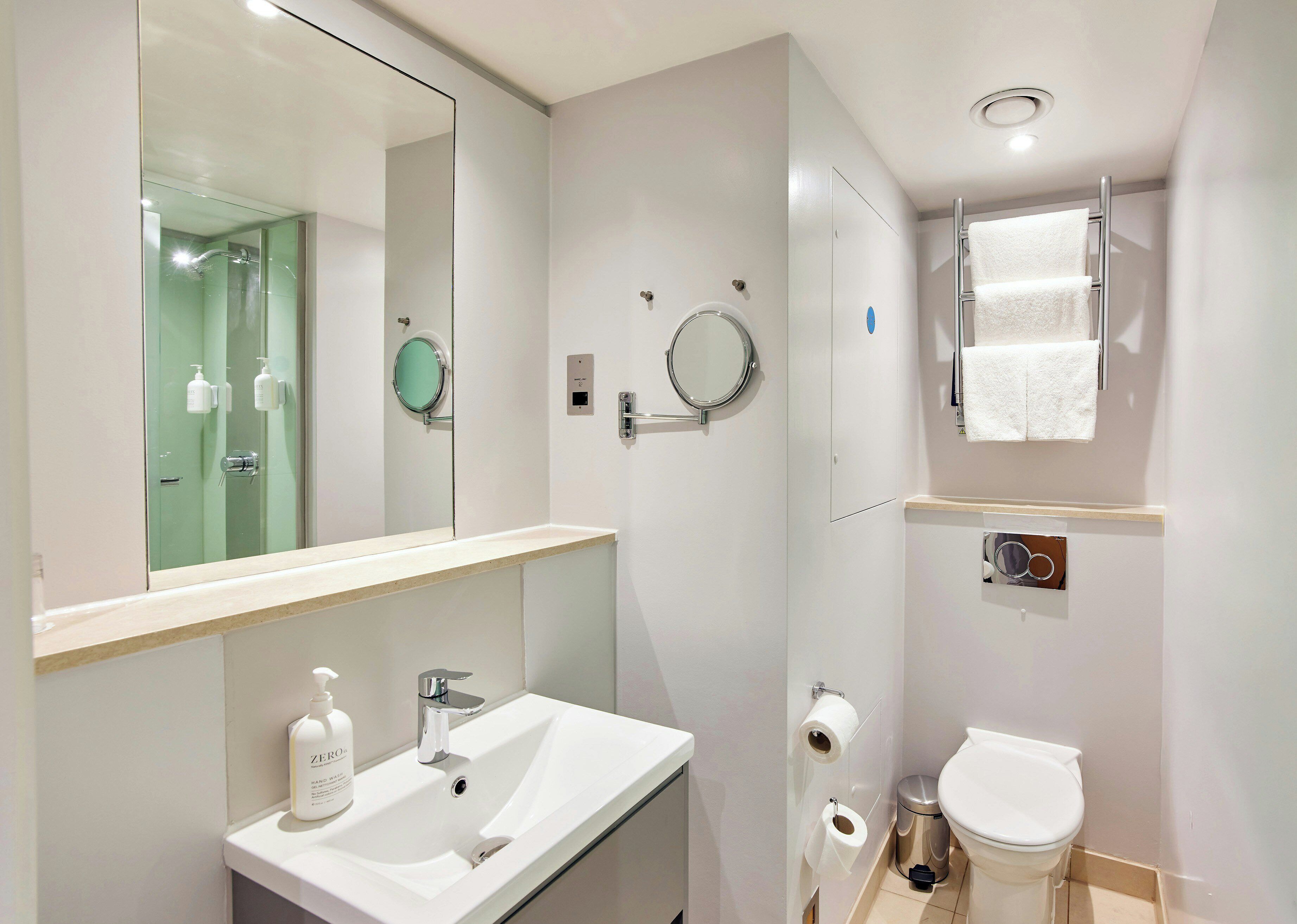 Een moderne badkamer met een grote spiegel, een wastafel, toilet en douche.