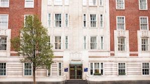A multi-story building with a symmetrical facade, featuring a central entrance with double doors and a sign above. - Thistle London Park Lane (London)