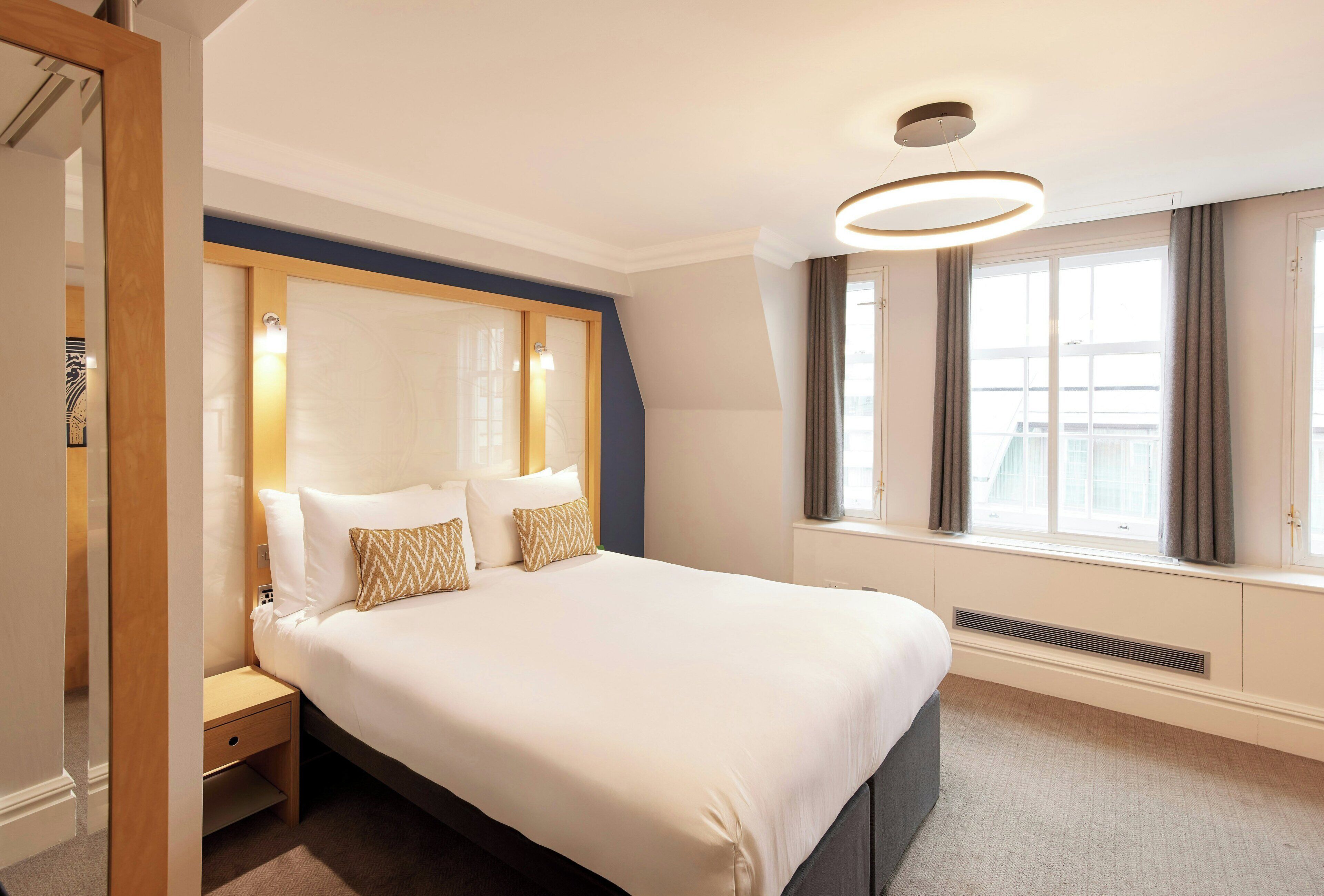 Ein Hotelzimmer mit einem großen Bett, Nachttischen, einem mit Vorhängen versehenen Fenster und einer modernen Deckenleuchte.
