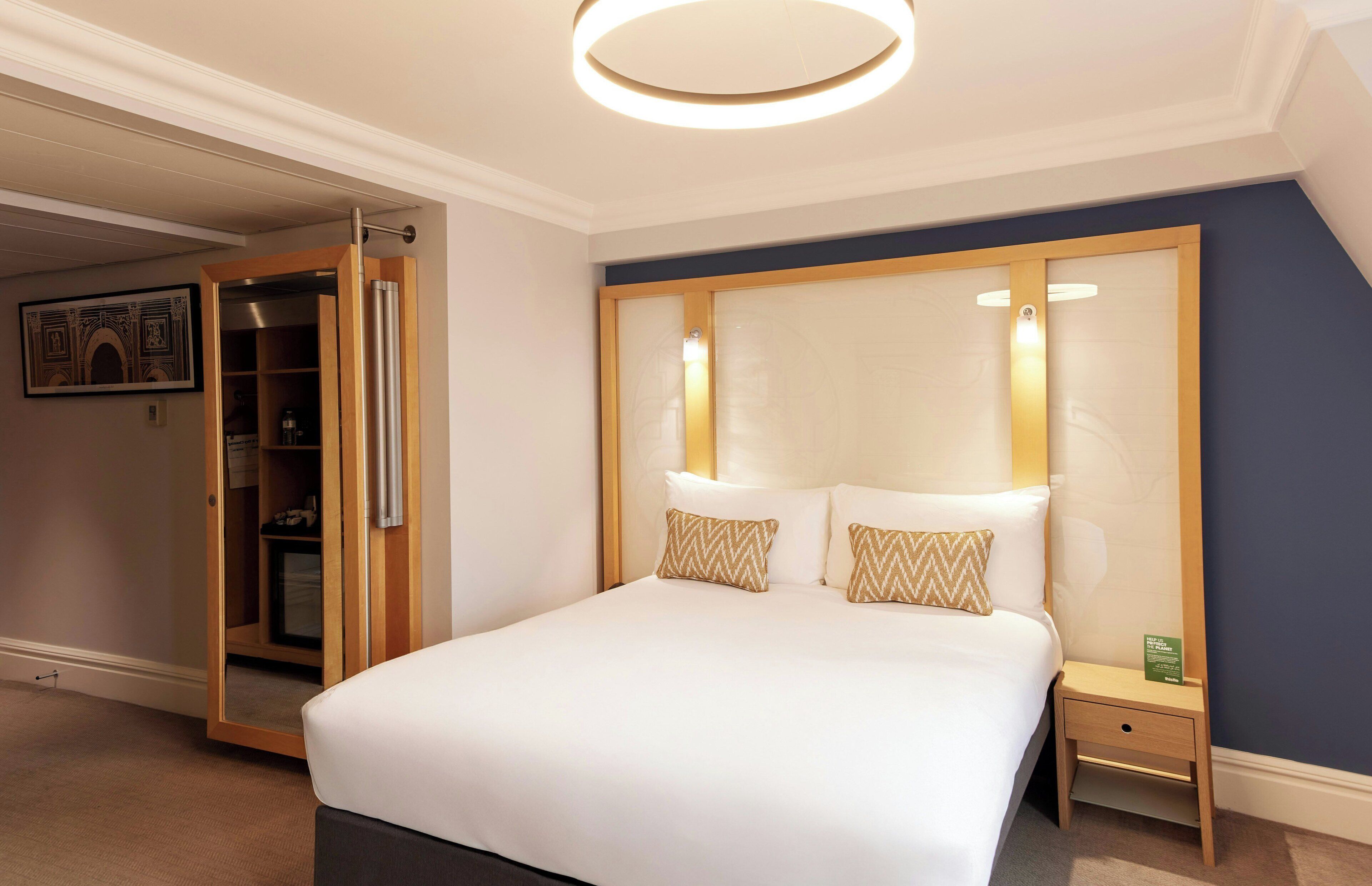 A neatly arranged hotel room with a bed, bedside table, and a wardrobe with a mirror.