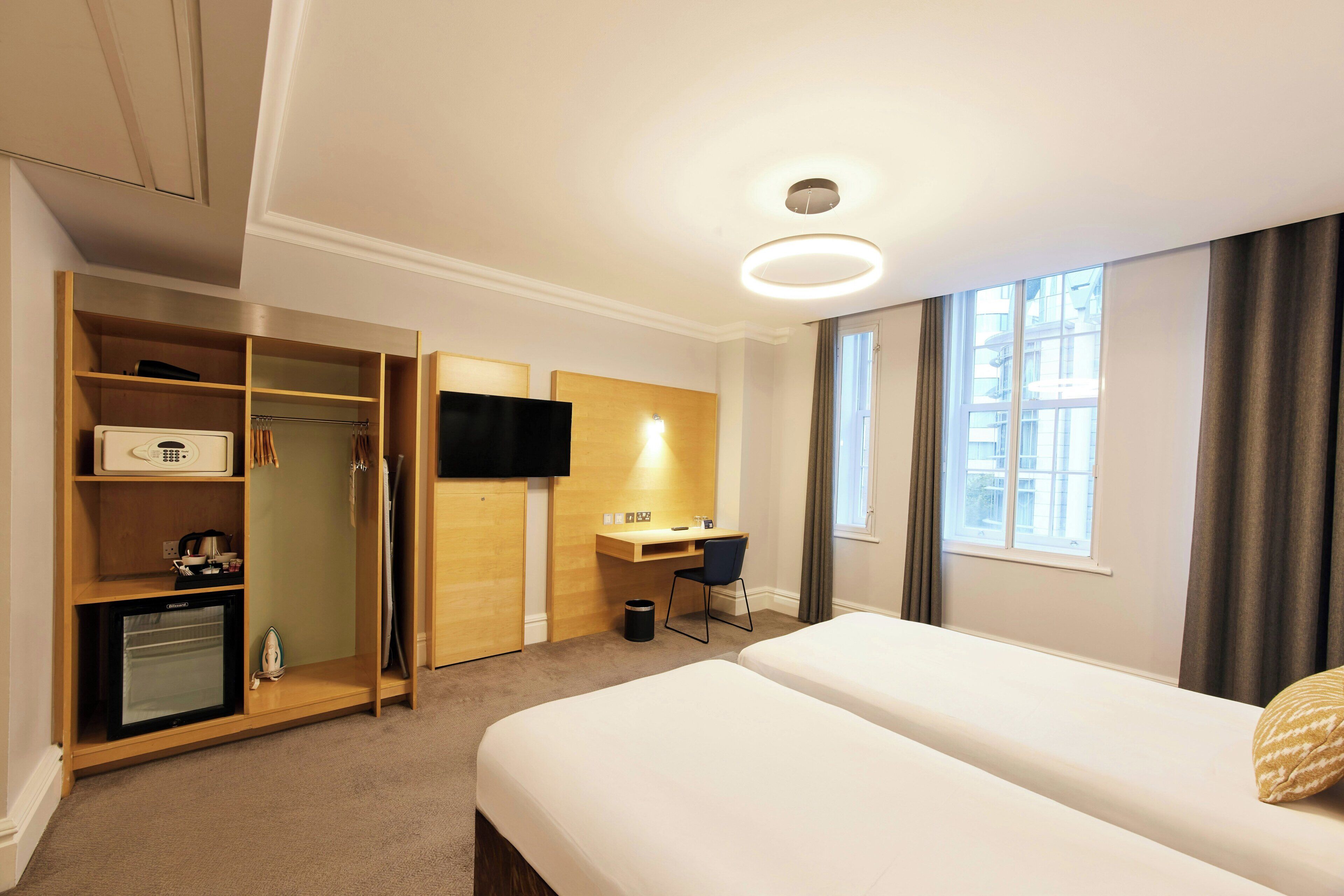A hotel room with a bed, a desk, a TV, a wardrobe, and a small kitchenette.