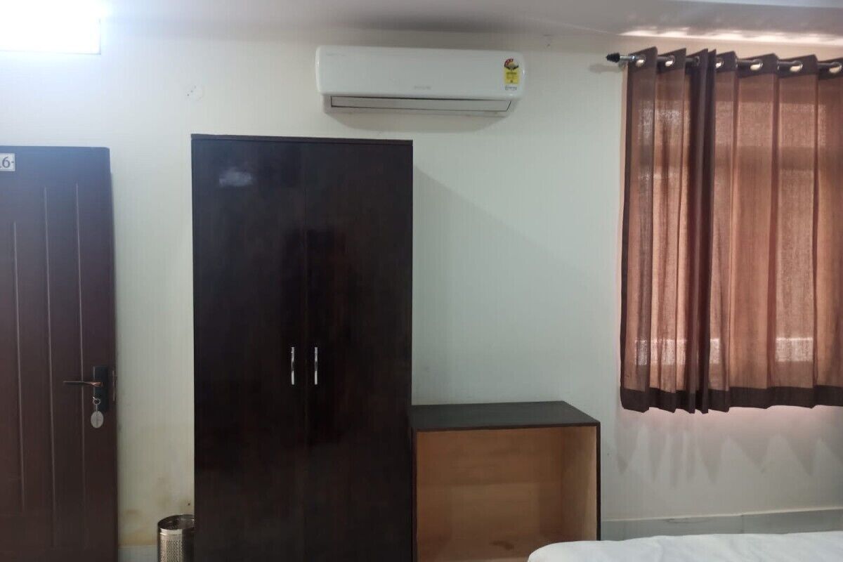 Una habitación con cama, armario, pequeño mueble y aire acondicionado en la pared.