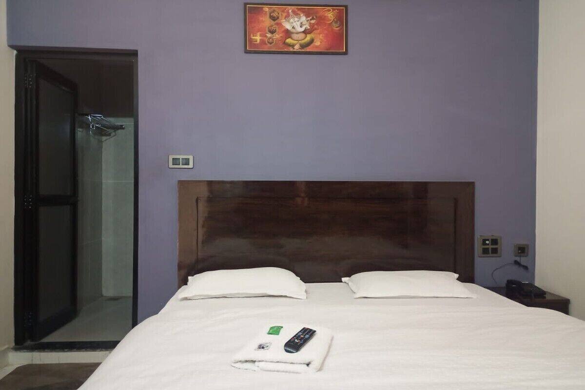 Une chambre d’hôtel avec une tête de lit en bois, un lit avec du linge de maison blanc, une télécommande et un tableau au mur.