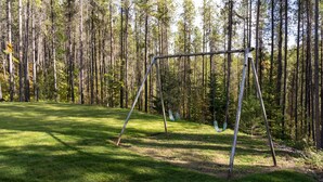Une balançoire installée dans un espace herbeux, entourée de grands arbres.