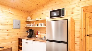 Une cuisine compacte aux murs en bois, dotée d’un réfrigérateur en acier inoxydable, d’un four à micro-ondes et d’une machine à café.