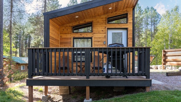 Une cabane en rondins moderne, dotée d’une terrasse, de grandes fenêtres et d’une porte.