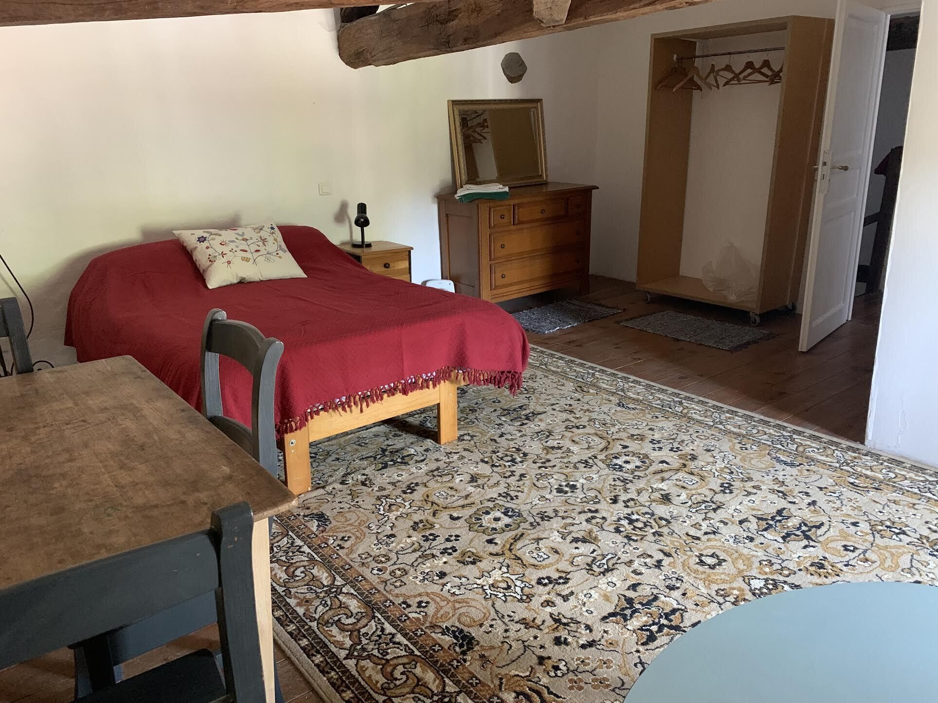 Une chambre à coucher avec un lit, une commode en bois, un miroir, une chaise et une table.