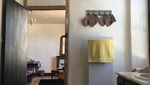 Een smalle gang met een houten deur, een handdoekrek met handdoeken, een radiator en een vloerkleed.