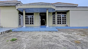 A building with a flat roof, a central entrance with steps, and a tiled ground. - Hotel O Firza Homestay (Palembang)