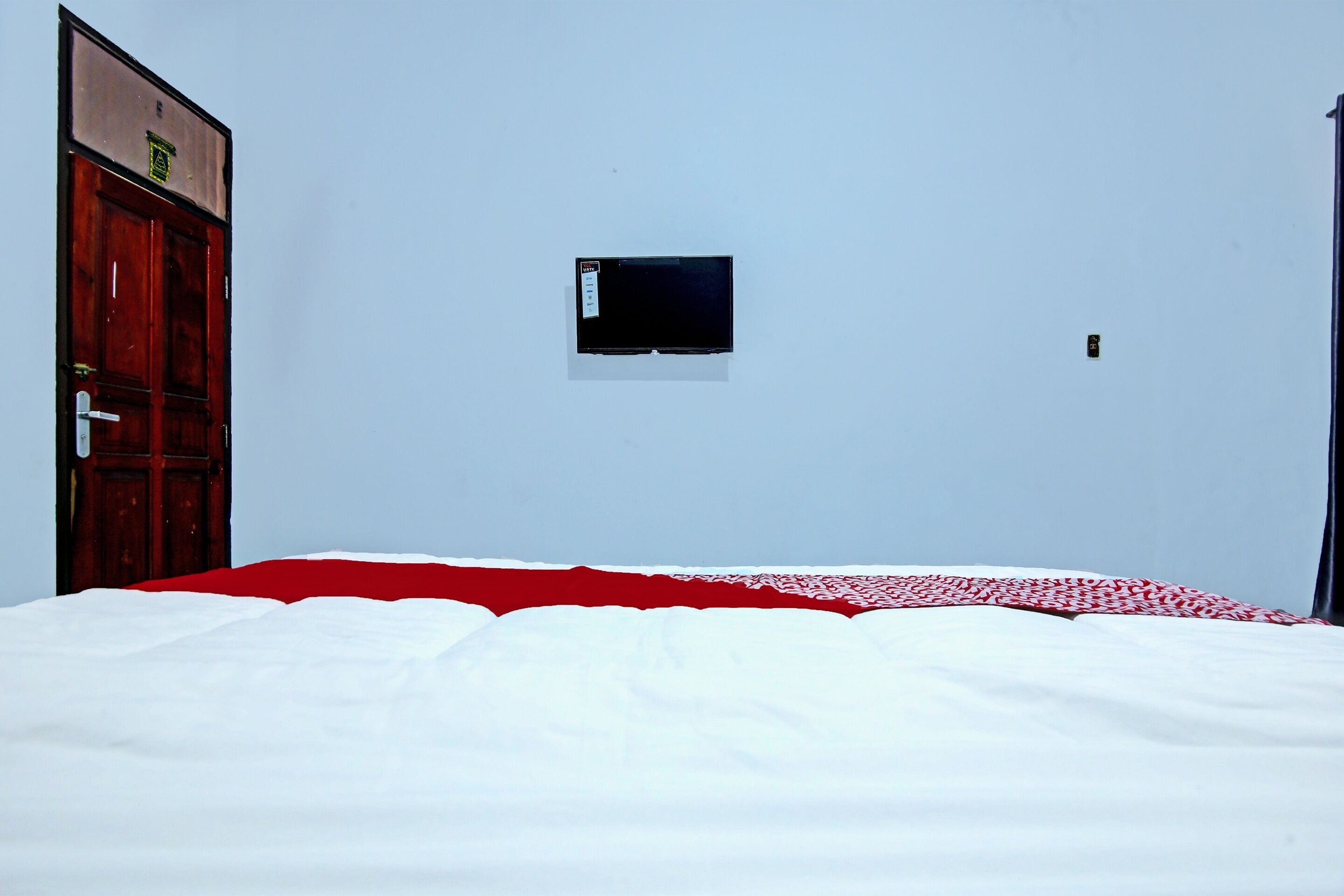 A room with a bed, a small TV mounted on the wall, and a door.