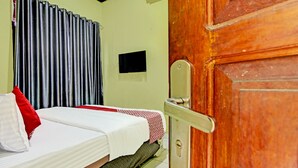 A room with a bed, a wooden door, a television on the wall, and a curtain. - Hotel O Firza Homestay (Palembang)