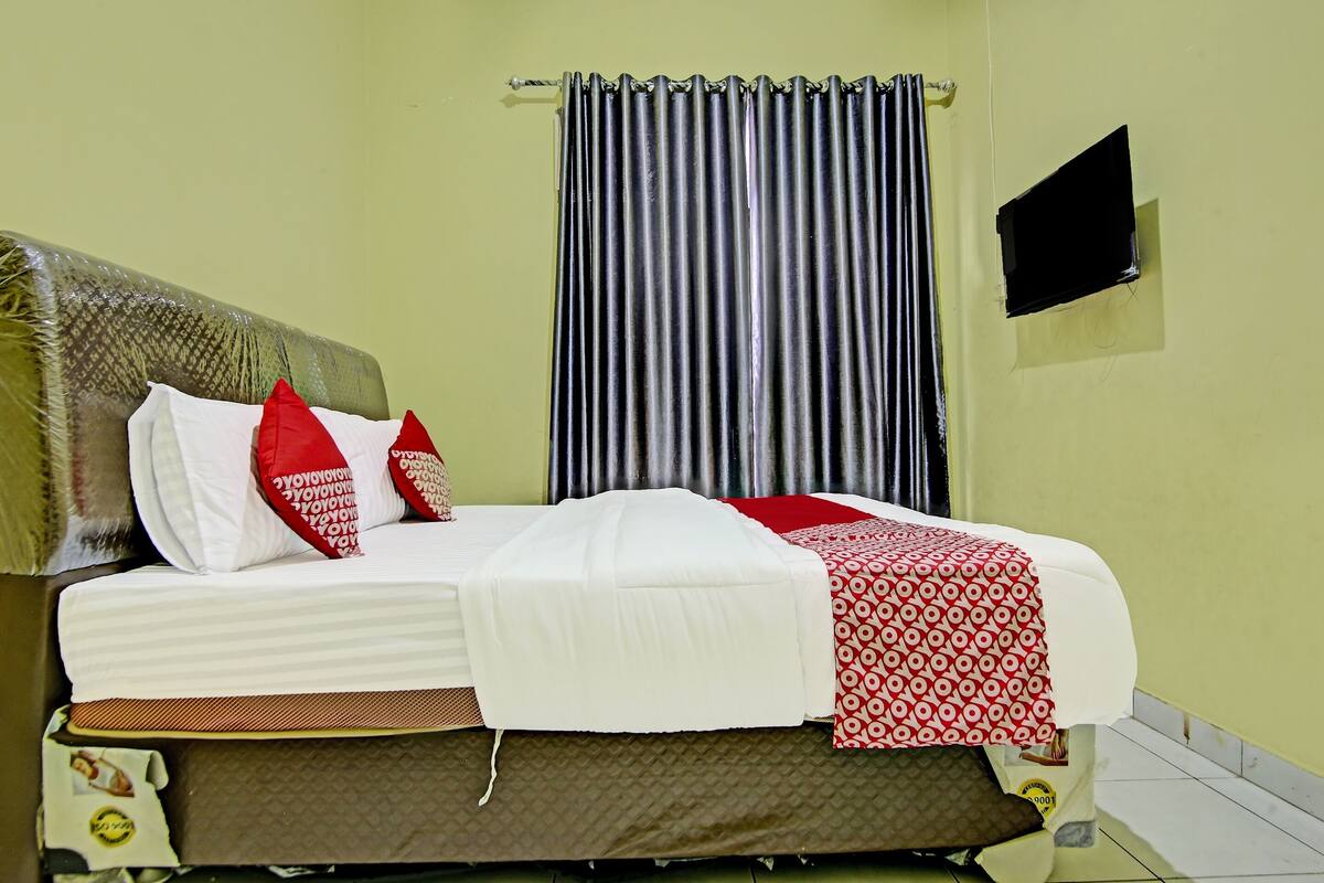 A neatly made bed with white and red bedding, a striped curtain, and a small TV mounted on the wall.