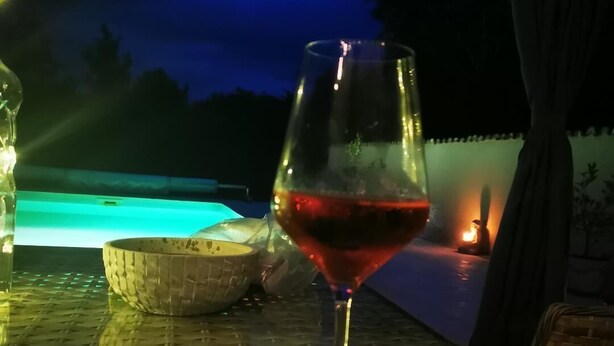 Un verre de vin rouge sur une table, avec une piscine en arrière-plan.