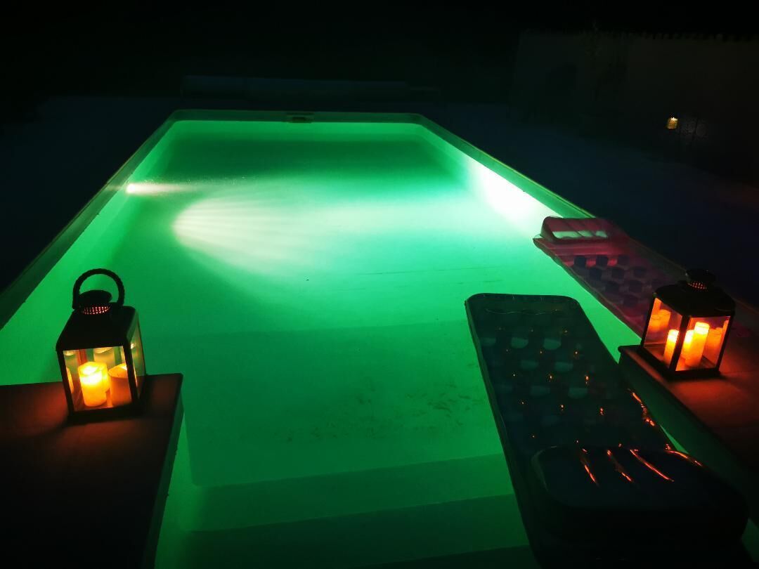 Un espace piscine avec un sol éclairé de lumière verte, deux lanternes et une télécommande posée sur un support.