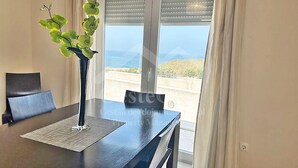 Ein modernes Zimmer mit einem dunklen Holztisch, einer schwarzen Vase mit grünen Blättern und Meerblick durch große Fenster.