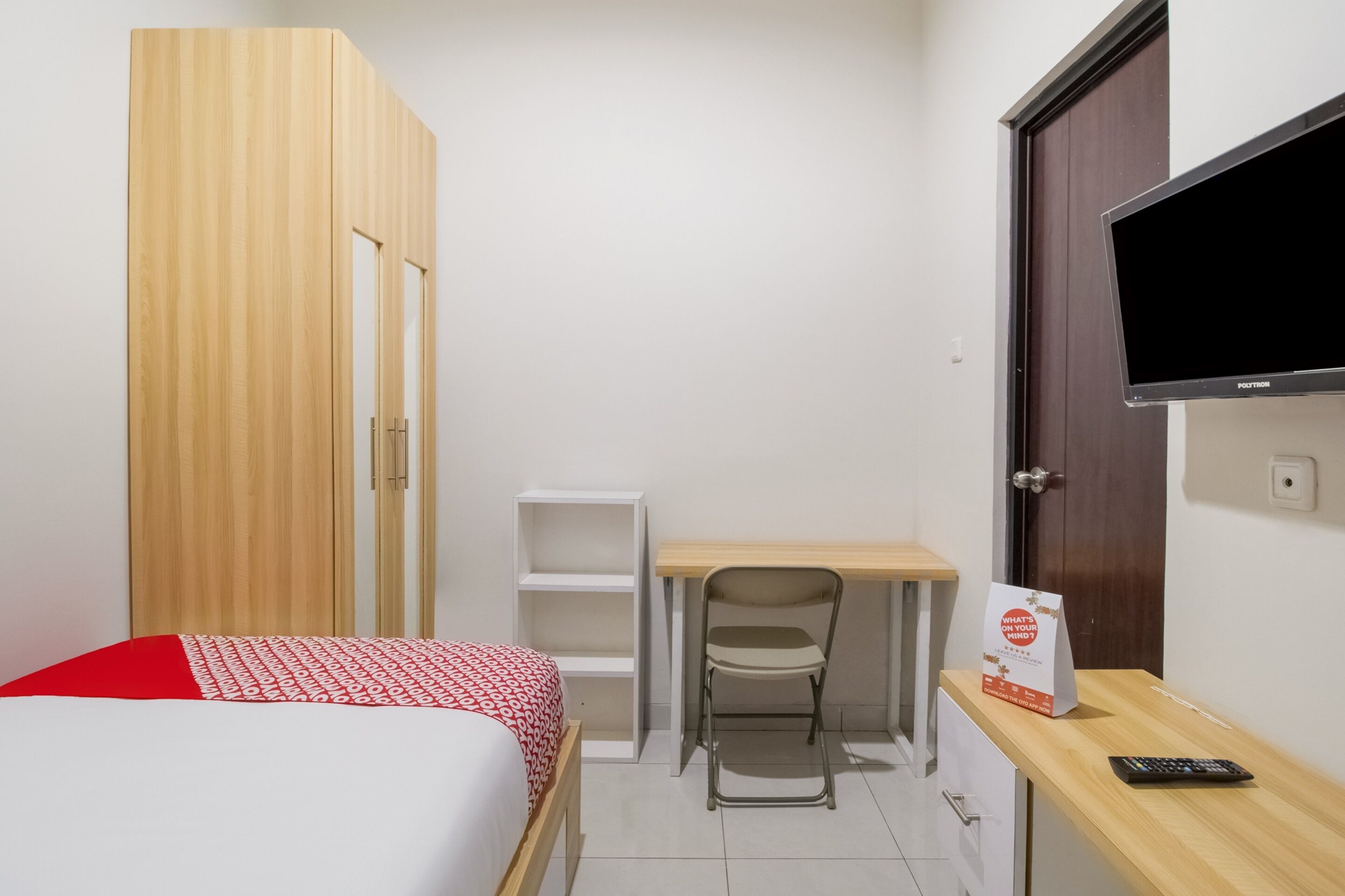 A small, neatly organized room with a bed, a desk, a chair, a TV, and a wardrobe.