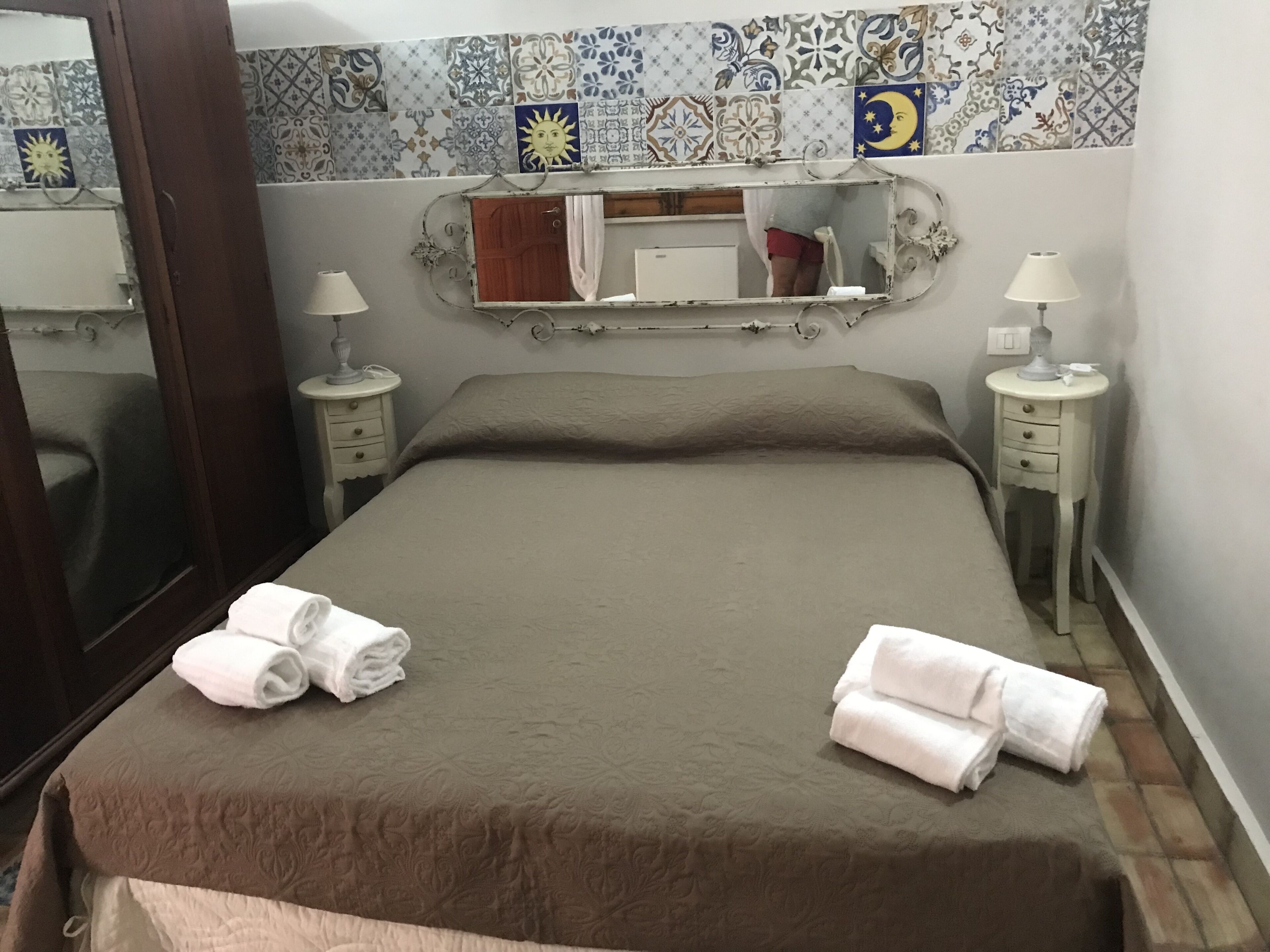 A neatly made bed with two towels, a mirror above it, and two bedside tables with lamps.